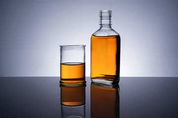 A backlit of a glass bottle and jar with golden liquid 