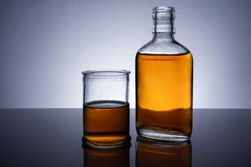 A backlit of a glass bottle and jar with golden liquid 