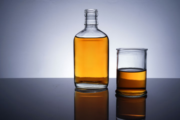 A backlit of a glass bottle and jar with golden liquid 