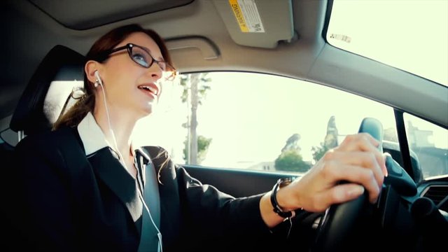 Attractive caucasian business woman driving while talking on the phone through her headphones. She concentrates on this serious business call. Slow motion.
