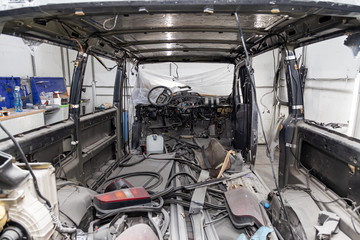 Car interior in the back of a van with a disassembled lining, seats removed, spare parts lying on the floor glass and rubber seal during preparation in a vehicle repair workshop. Auto service industry
