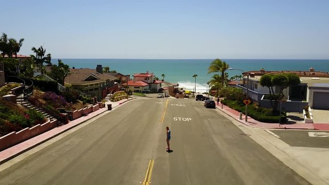 A girl riding a skateboard down a small hill near a Southern Californian Beach.