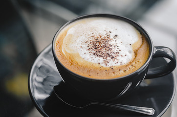 close up modern hot black coffee the cappuccino on dark background with coffee bubble foam pattern and texture in black cup looking and feel so delicious on glasses table in coffee shop.