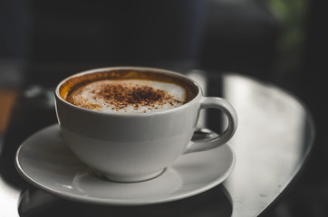 close up modern hot black coffee the cappuccino on dark background with coffee bubble foam pattern and texture in white cup looking and feel so delicious on glasses table in coffee shop.