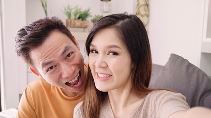 Asian couple using smartphone VIDEO Call with friend in living room at home, sweet couple enjoy love moment while lying on the sofa when relaxed at home. Lifestyle couple relax at home concept.