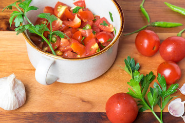 Tomato salad with basil, olive oil, garlic, chilli and balsamic vinegar in bowl over wooden background
