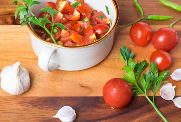 Tomato salad with basil, olive oil, garlic, chilli and balsamic vinegar in bowl over wooden background