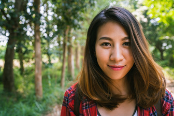 Naklejka premium Happy young Asian woman traveler with backpack walking in forest. Hiker Asian woman with backpack walking on path in summer forest. Adventure backpacker travel people concept.