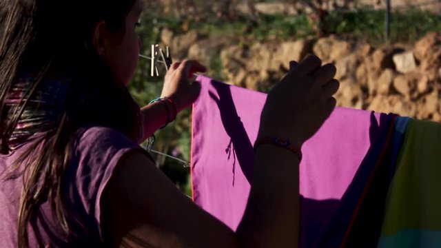A girl hanging a purple towel to dry outside with a clothespin on a clothesline on a hot day