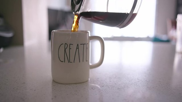 Coffee pot pouring coffee into a mug with "CREATE" on it before a hand pulls the mug out of frame