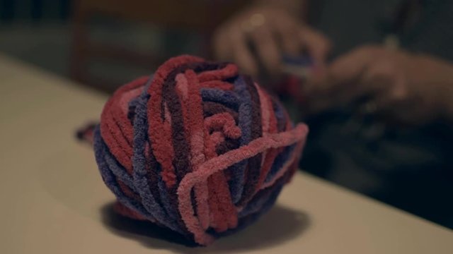 Young woman knitting with stitches a colorful craft in a cozy autumn day on the background with the knitting wool ball in the foreground.