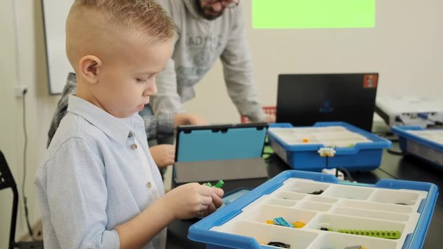 Curious blond caucasian kid experiences how to construct the plastic robot toy at the class slow motion