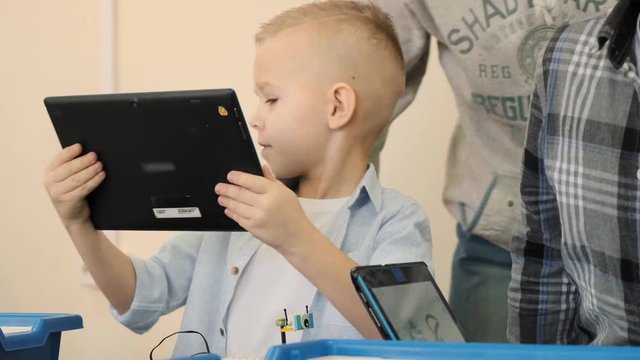 Attentive teacher explains to the young blond boy how to make the robot cat from plastic details and using new technologies slow motion