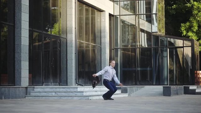 cheerful businessman in shirt checks time and jumps with joy from office building steps in modern summer city