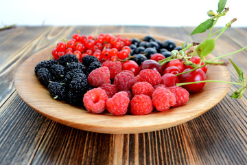 Different delicious fresh summer berries cherry, currant, blackberry in wooden plate on wooden background 
