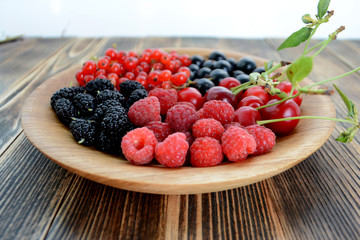 Different delicious fresh summer berries cherry, currant, blackberry in wooden plate on wooden background 