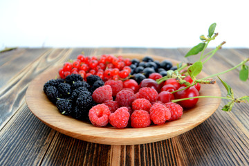 Different delicious fresh summer berries cherry, currant, blackberry in wooden plate on wooden background 