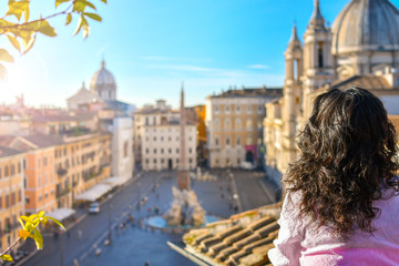 A woman stands on a rooftop terrace overlooking the Piazza Navona and fountain on a sunny summer...