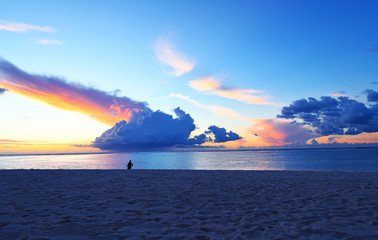 EVENING TWILIGHT CLOUD SKY OVER LOW TIDE BEACH SAND AT ISLAND SEASIDE with SILHOUETTE of the Fisheman