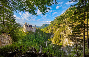 Bavaria, Germany. Fairytale Neuschwanstein Castle in Bavarian Alps mountains. Picturesque view from green forest trees, lake and sunrise sky with clouds. Famous landmark and touristic travel.