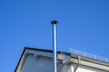 Stainless steel chimney and parts of a roof in front of a bright blue sky.