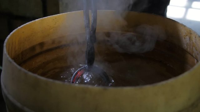 Metallic rose is placed into a pot with beeswax to cool it in an old workshop  
