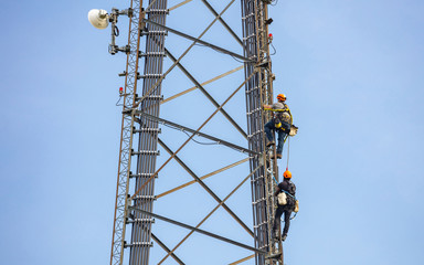 Telecom maintenance. Two repair men climbing on tower against blue sky background