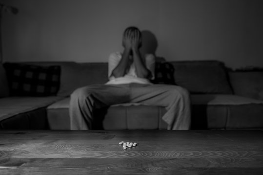Depressed man suffering from suicidal depression want to commit suicide by overdose strong medicament drugs and pills pain killers while he sitting in dark room selective focus moody dramatic look