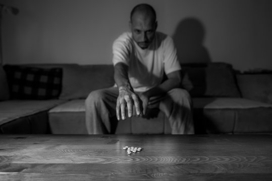 Depressed man suffering from suicidal depression want to commit suicide by overdose strong medicament drugs and pills pain killers while he sitting in dark room selective focus moody dramatic look