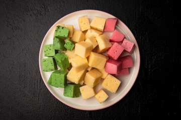 Cheese cubes of green, yellow and red on a plate. Top view