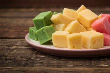 Set of multicolored cheese on a plate, wooden background. Wine appetizer. Copy space