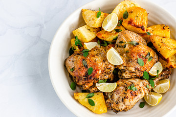 Greek Lemon Chicken with Potatoes in a Bowl on White Background. Baked Chicken and Potatoes Garnished with Fresh Oregano Leaves Directly from Above Photo.