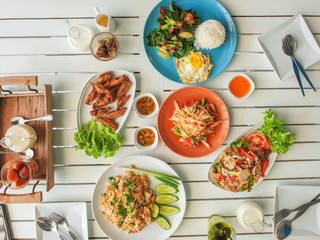 Top view Food with Fried rice with eggs, vegetables, papaya salad Fried Chicken and Fried Kale, Thai pork sausage salad On a white wooden table
