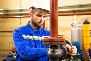 Worker on industrial plant. Technician operator turning gate valve on boiler system. Man in helmet...