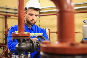 Technician worker on heating system. Station operator opens water valve on pipeline. Man works on...