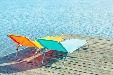 Two empty bright sunbeds on wooden pier by the river. Concept of tourism and recreation. 