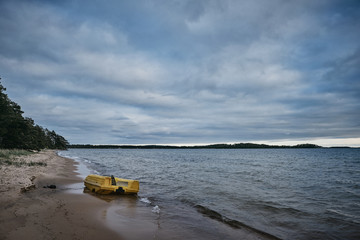 Fototapeta na wymiar yellow pedal boat floating ashore up and down the beach, dark clouds on the sky and beach in the foreground