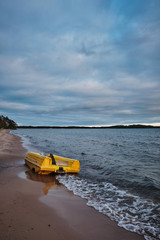 yellow pedal boat floating ashore up and down the beach, dark clouds on the sky and beach in the foreground