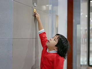 Fototapeta na wymiar Little Asian baby girl, 3 years old, reaching her hand out to try pushing the elevator button - children development by allowing them to help doing things in everyday life