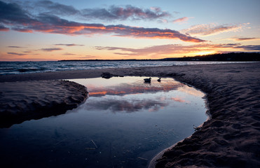 a stream leads out to a lake during sunset with reflections in the water and two ducks swimming in the stream