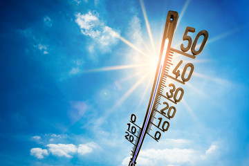 Hot summer or heat wave background, bright sun on blue sky with thermometer