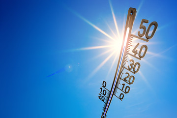 Hot summer or heat wave background, bright sun on blue sky with thermometer