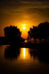 Beautiful silhouette of sun rising in Rhodes, Greece. The image shows bamboo sunshades and trees. The sun is reflected from the pool.