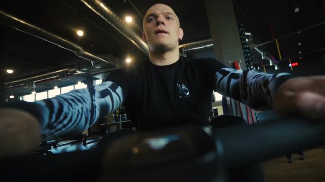bald muscular man in professional tracksuit does seated cable rows in modern gym low angle shot slow motion