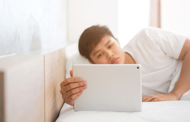 close up young asian man playing tablet on bed in weekend	