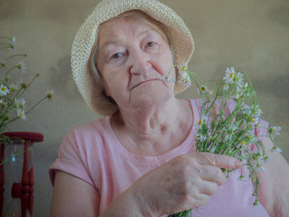 Elderly woman with bouquet of medical daisies in pink T-shirt and hat. Pensioner engaged in...