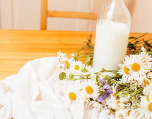 Simply stylish wooden kitchen with bottle of milk and glass on table, summer flowers camomile, healthy foog moring concept