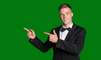 Handsome man in suit points his fingers left isolated on green background.