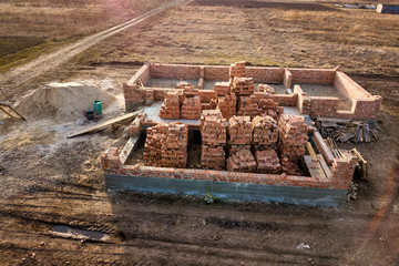 Aerial view of building site. Trenches dug in ground and filled with cement as foundation for future house, brick basement floor and stacks of brick for construction.