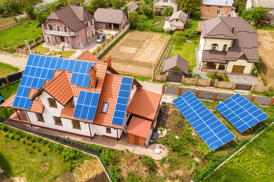 Aerial top view of new modern residential house cottage with blue shiny solar photo voltaic panels system on roof. Renewable ecological green energy production concept.